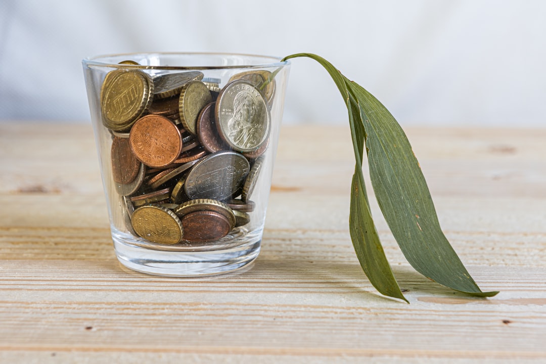 Young person using smartphone to check investment app with coins and small bills nearby