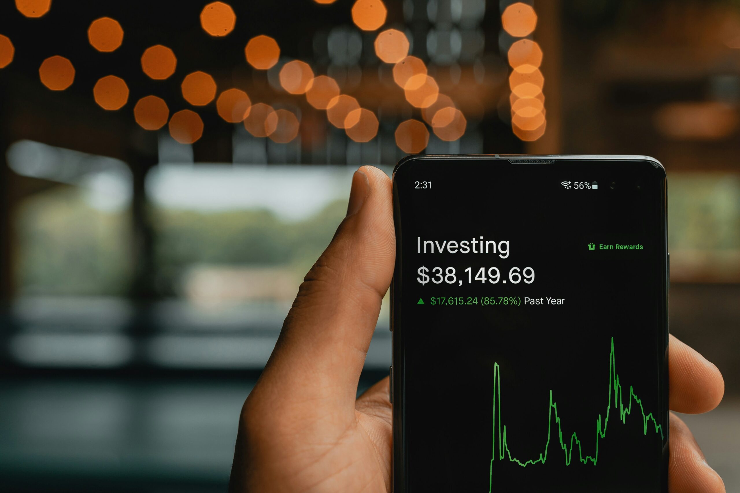 Hand holding phone showing investing app with $38,149; difference between saving and investing