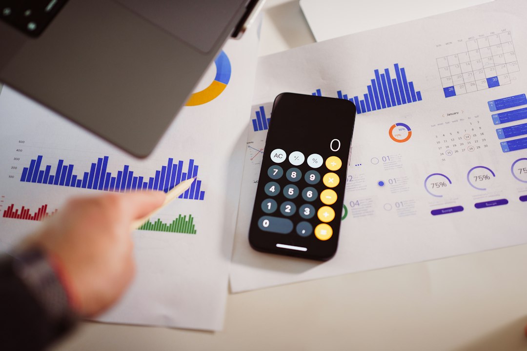 Hand writing expense amounts in a notebook next to a calculator and receipts
